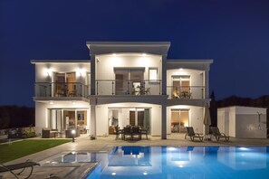 Ein modernes, zweistöckiges Haus mit Swimmingpool, Sitzgelegenheiten im Freien und einer überdachten Terrasse.