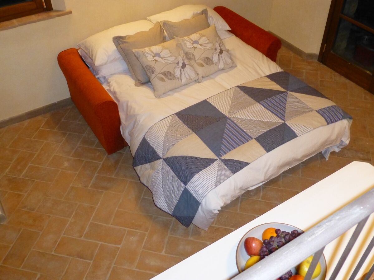 Una cama con una colcha de estampado geométrico, una silla roja y un frutero sobre una mesa.