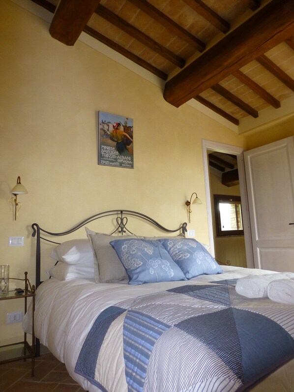 Un dormitorio con cama, mesita de noche, lámpara, un cartel en la pared y una puerta a otra habitación.