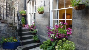 A stone building with a staircase leading to a door, surrounded by potted plants and flowers. - Stylish Apartment in Edinburgh City Centre, Sleeps 4. License no. EH-68704-F (Edinburgh)