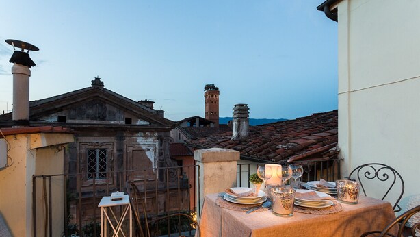 A terrace with a table set for dining, a lantern, and a view of historic buildings. - CASA MARGHERITA Stunning view from Terrace (Lucca)