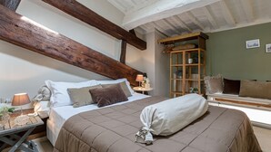 A bedroom with a large bed, wooden beams, a wooden cabinet, and a small table with a lamp. - CASA MARGHERITA Stunning view from Terrace (Lucca)