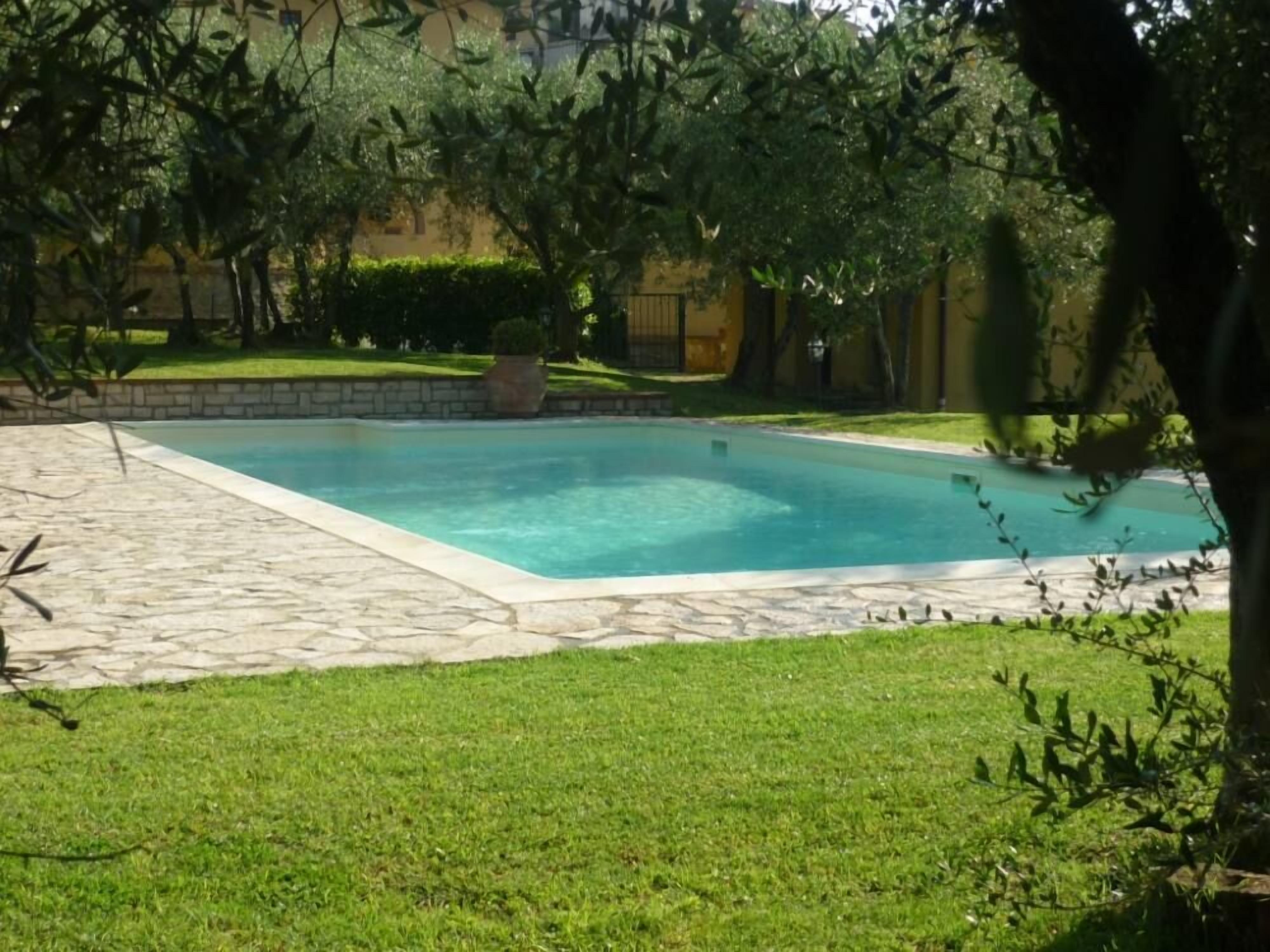 A rectangular swimming pool with a stone deck and a grassy area in front.