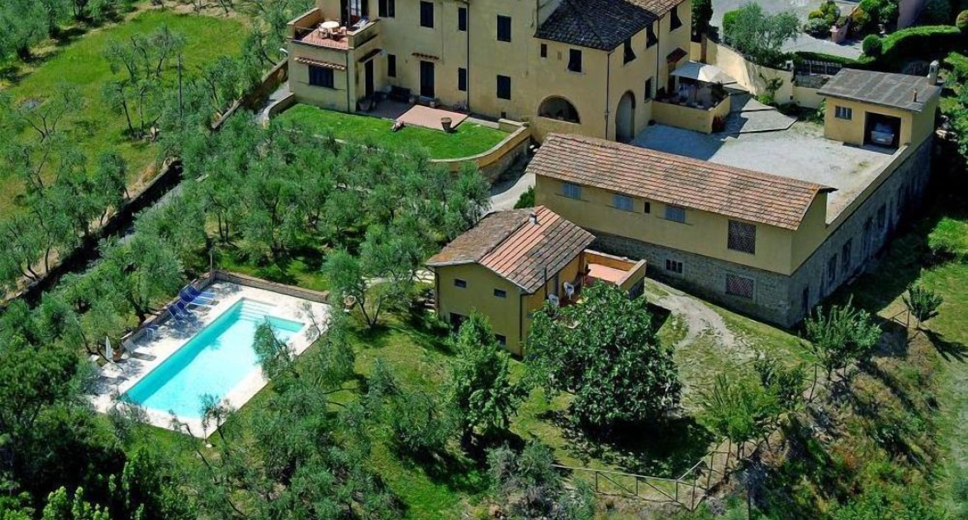 Un edificio grande de varios pisos con piscina, rodeado de abundante vegetación.