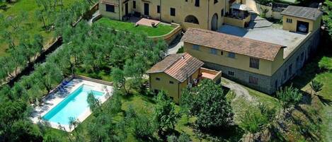 Un edificio grande de varios pisos con piscina, rodeado de abundante vegetación.