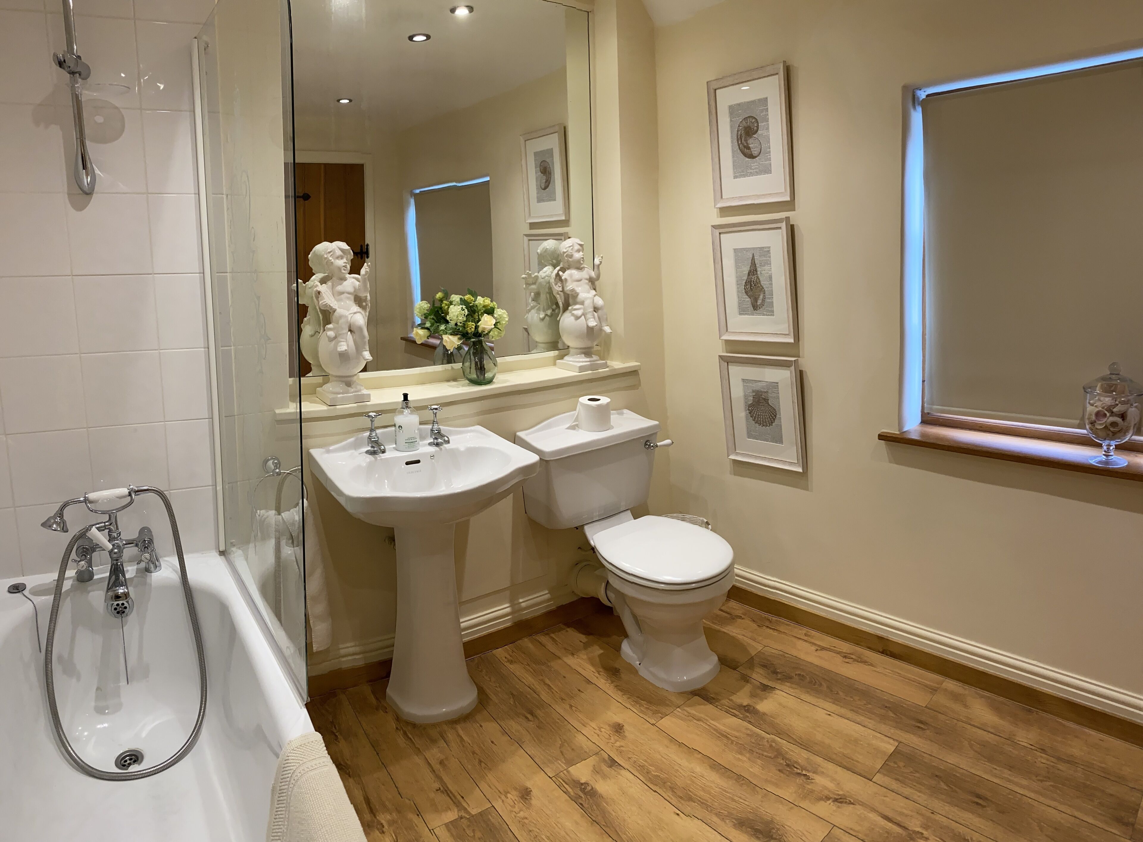 A bathroom with a bathtub, a sink, a toilet, and a mirror. There are framed pictures on the wall and a window with blinds.