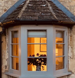 Ein Eckfenster mit Blick in einen Raum, der ein Bett und eine Blumenvase zeigt.