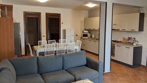 Una sala de estar moderna con un sofá gris, una mesa de comedor con sillas y una zona de cocina con armarios y electrodomésticos.