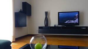 A modern living room with a flat-screen TV, a dark wooden cabinet, and a glass fishbowl with an apple on a black coffee table. - Beach front apartment with superb sea view, 10 min. from Porto   (Vila Nova de Gaia)