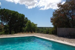 Une piscine rectangulaire à l’eau d’un bleu limpide, entourée d’une terrasse en pierre et d’une clôture en bois.
