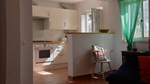 A compact kitchen with white cabinets, a stove, and a window with a green curtain. - Azeitao: Holidays Villa with pool and beach nearby (Azeitão)