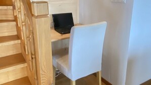 Portaat, joissa on puiset kaiteet, johtavat huoneeseen, jossa on valkoinen tuoli ja pöytä, jonka päällä on kannettava tietokone.