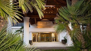 The entrance of Sands Beach Resort with a sign above the doors, surrounded by palm trees and a covered area with string lights. - Beautiful beachside apartment with stunning sea views. Seven pools on complex! (Costa Teguise)