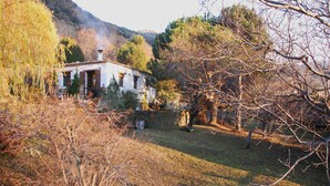 A rustic house with a stone wall, a wooden door, and a chimney emitting smoke. - Country House and garden on Edge of Picturesque Village,LGBTQ+friendly (Bubion, Granada)