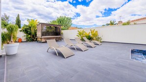 Une terrasse sur le toit aménagée avec des chaises longues, un espace barbecue et des plantes en pot.