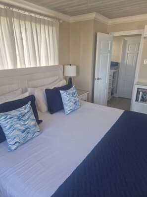 A neatly made bed with a white and blue patterned pillow, a bedside lamp, and a white door leading to a bathroom. - Beachfront Apartment at Dover Beach, St Lawrence (St Lawrence,)
