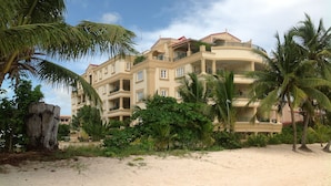 Ett hotell vid stranden med flera balkonger, palmer och en sandstrand.