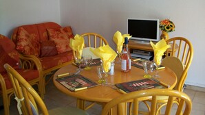 A dining area with a wooden table set for two, surrounded by yellow chairs. A television is mounted on the wall above the table. - Family friendly villa only 5 minutes walk to the Cap d'Agde beach (Richelieu) (Agde)