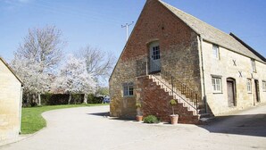A stone building with a steeply pitched roof, a small balcony, and a staircase leading to the entrance. - Boddingtons Barn in the Cotswolds  (1 Bedroom) (Gloucestershire)