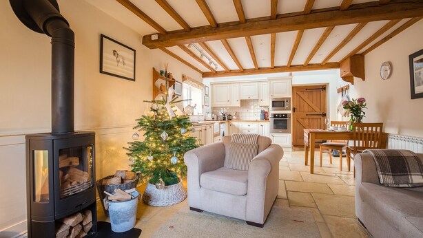 A cozy living room with a fireplace, a Christmas tree, and a dining area with a wooden table and chairs. - Boddingtons Barn in the Cotswolds  (1 Bedroom) (Gloucestershire)