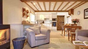 A cozy living room with a fireplace, a sofa, and a dining area with a table and chairs. - Boddingtons Barn in the Cotswolds  (1 Bedroom) (Gloucestershire)