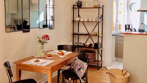 Uma área de refeições com uma mesa de madeira, cadeiras e uma estante com utensílios de cozinha.