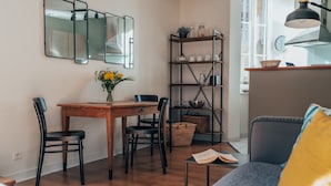 Ett kompakt vardagsrum med ett matbord i trä, två stolar, en soffa, en bokhylla och ett litet sidobord.