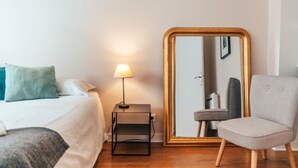 Quarto de hotel com cama, mesa de cabeceira com luminária, um espelho grande e uma cadeira.