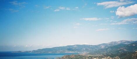 A coastal landscape with a clear sky, a large body of water, and distant mountains.