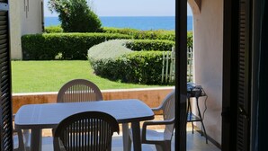 Une terrasse ouverte avec une table et des chaises, une vue sur la mer et un jardin bien entretenu.