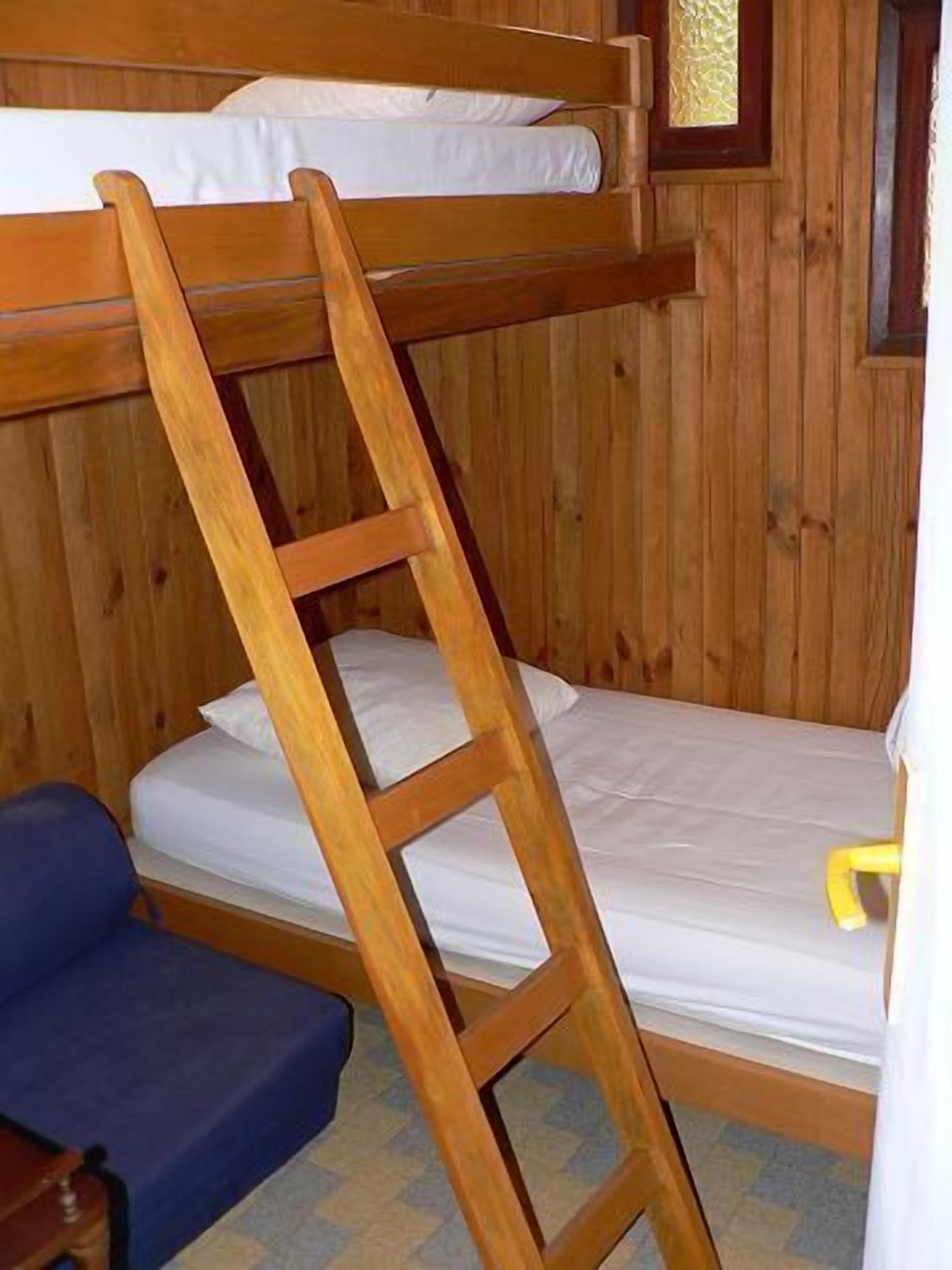 A bunk bed with a wooden ladder, a blue chair, and a small table.