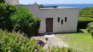 Un petit bâtiment avec une porte marron, entouré d’une végétation luxuriante et offrant une vue sur la mer.