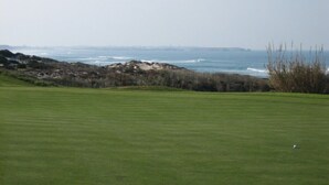 Ein Golfplatz mit Blick auf den Ozean und felsigem Hintergrund.