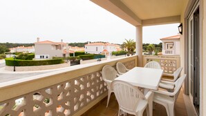 Ein Balkon mit einem weißen Tisch und Stühlen, einem Zierzaun und Blick auf angrenzende Häuser.