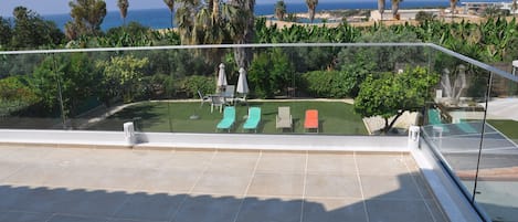 A rooftop terrace with a clear view of the ocean, palm trees, and a pool area with lounge chairs.