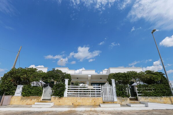 Una casa moderna con fachada blanca, entrada protegida por una reja y cielo azul despejado.