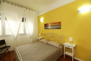 Un dormitorio con una cama, dos mesitas de noche, una silla y un cuadro en la pared.
