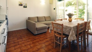 Een woonkamer met een bank, een eettafel met stoelen, een keukenhoek en een schuifpui naar een balkon.