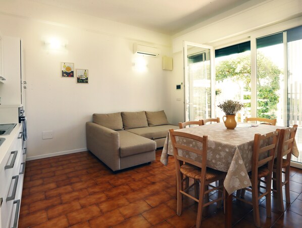 A living room with a sofa, a dining table with chairs, a kitchen area, and a sliding glass door leading to a balcony. - Seafront apartments Baia di Punta Prosciutto_A CASA DI TERESA (Lecce)