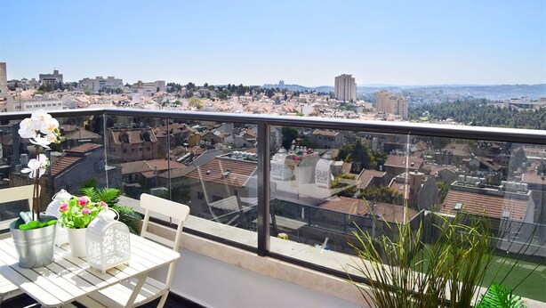 A balcony with a table and chairs, overlooking a cityscape with buildings and greenery. - ☆ Sublime apartment in the heart of Jerusalem ☆ (Jerusalem)