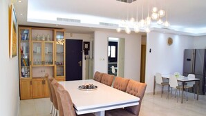A modern dining area with a white table and brown upholstered chairs, a chandelier, and a kitchen in the background. - ☆ Sublime apartment in the heart of Jerusalem ☆ (Jerusalem)