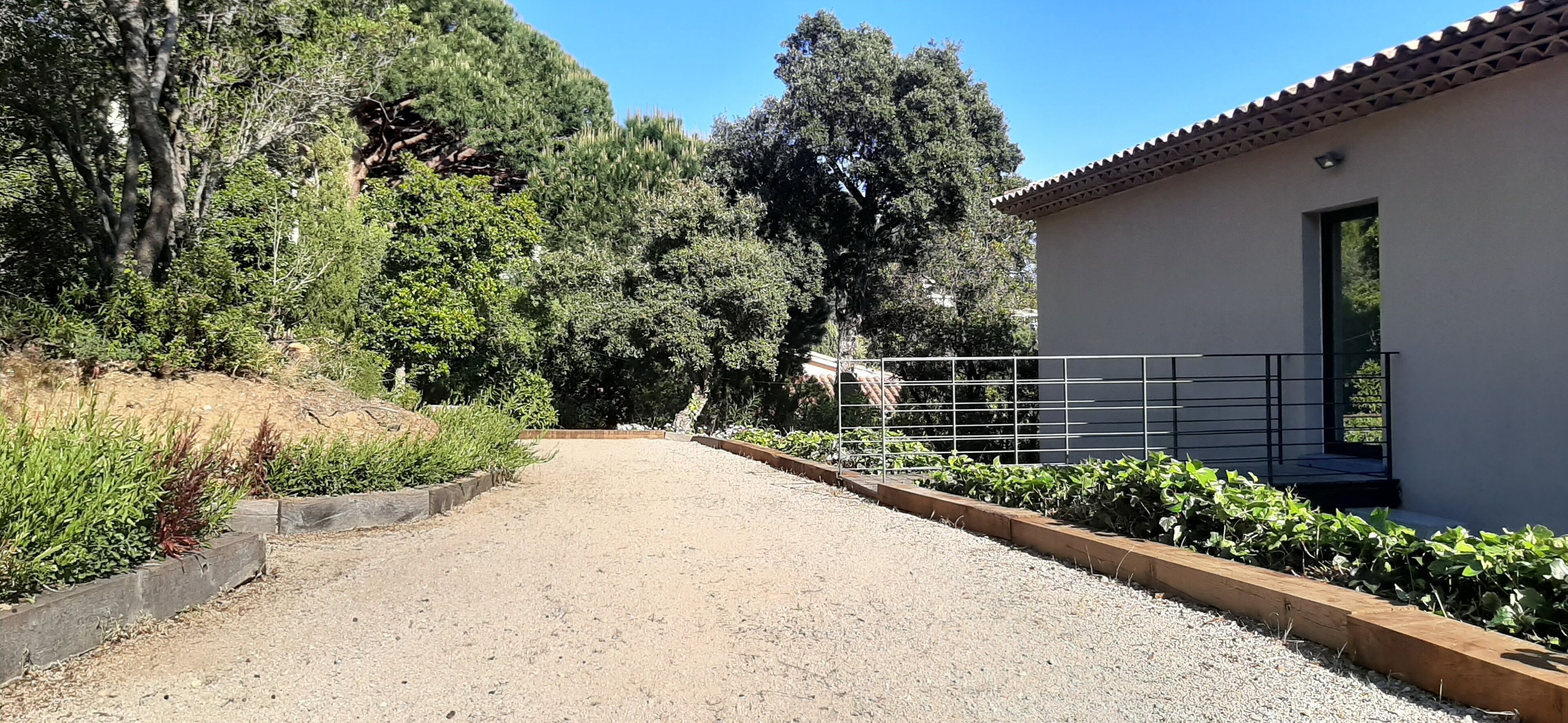 A gravel driveway leading to a building with a tiled roof and a metal railing.