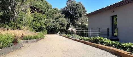 A gravel driveway leading to a building with a tiled roof and a metal railing.