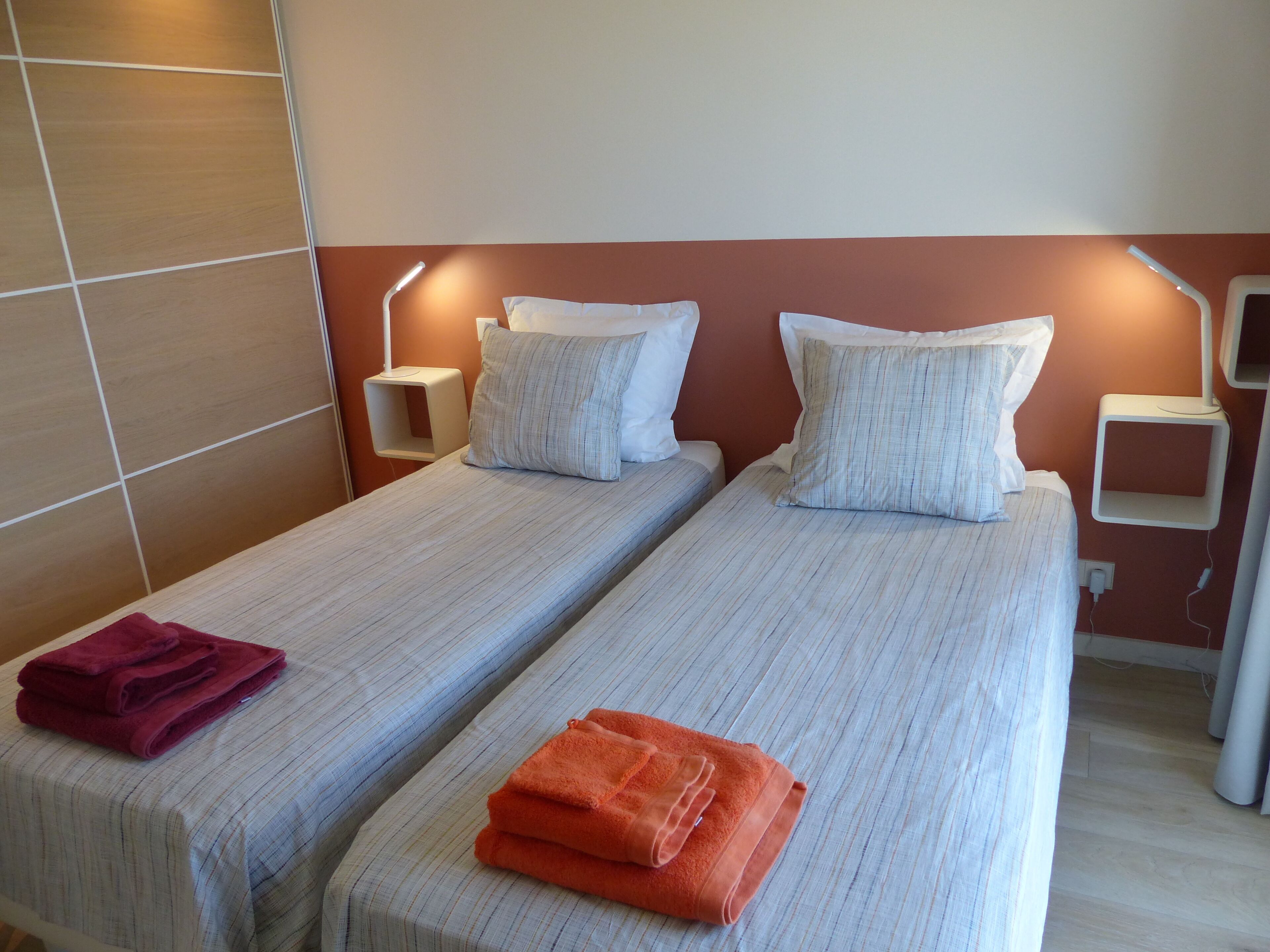 A hotel room with two single beds, each with a pillow and a folded towel.