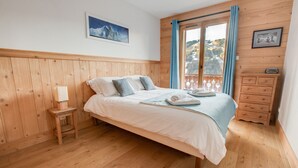 A bedroom with a wooden headboard, a bed with white bedding, a nightstand with a lamp, a dresser, and a window with curtains. - Modern 4 bed Chalet, Hot tub, Stunning views of Morzine, easy access to Avoriaz (Morzine)