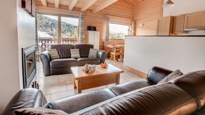 A cozy living room with a wooden ceiling, a fireplace, a sofa, and a dining area with a view of the mountains. - Modern 4 bed Chalet, Hot tub, Stunning views of Morzine, easy access to Avoriaz (Morzine)