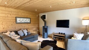Un accogliente soggiorno con soffitto in legno, camino, divano e televisione a parete.