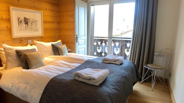 Camera d'albergo con soffitto in legno, un letto grande con lenzuola bianche, una coperta grigia e un quadro incorniciato appeso al muro.