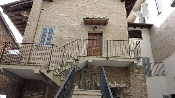 A two-story building with a wooden door, a balcony with metal railings, and a staircase leading to the upper floor. - Attic in the center of Assisi (Assisi)