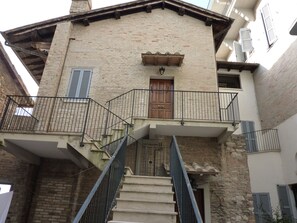 A two-story building with a wooden door, a balcony with metal railings, and a staircase leading to the upper floor. - Attic in the center of Assisi (Assisi)